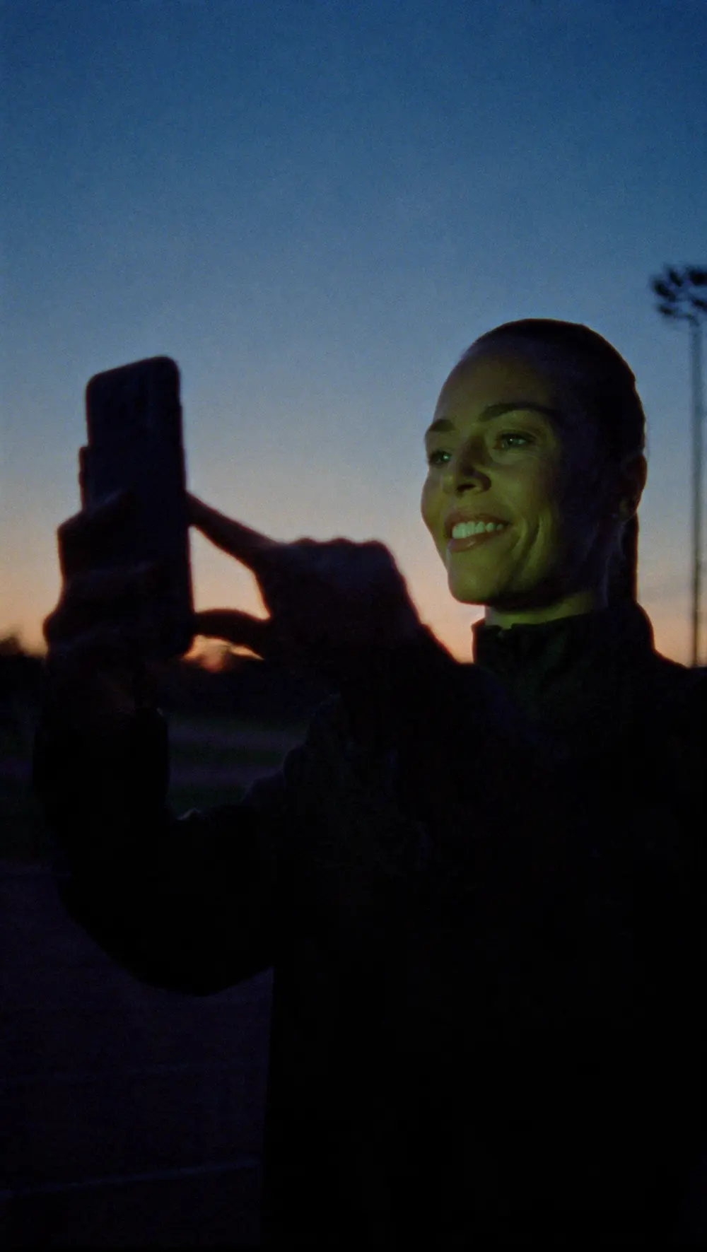 A coach holding up a phone at the track at sunset